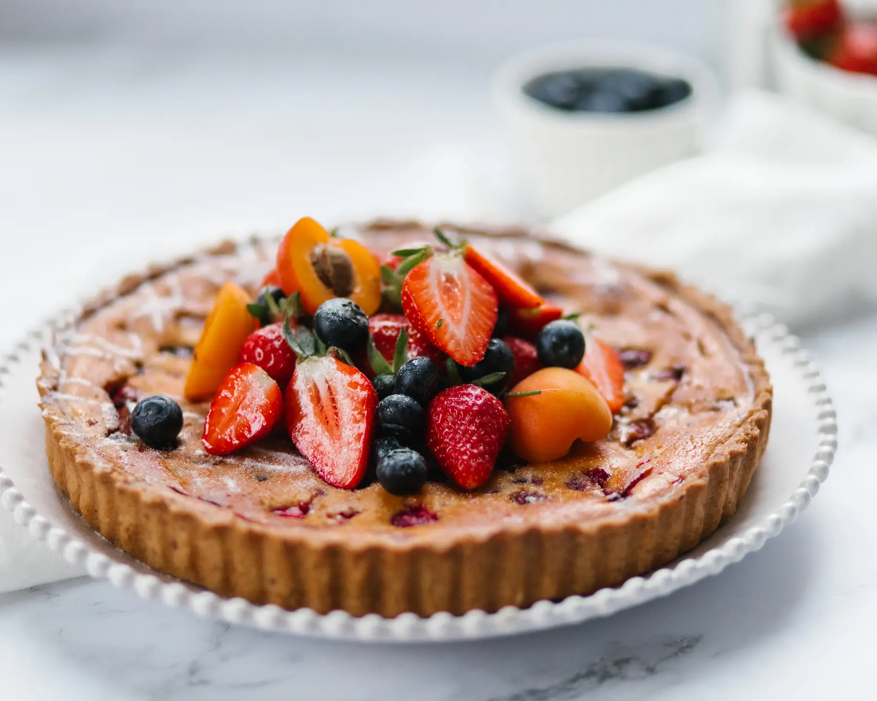 Simple Summer Berry and Frangipane Pie A round pie with berries is on the table. It has a golden brown crust. The pie is decorated with berries. Horizontal photo.