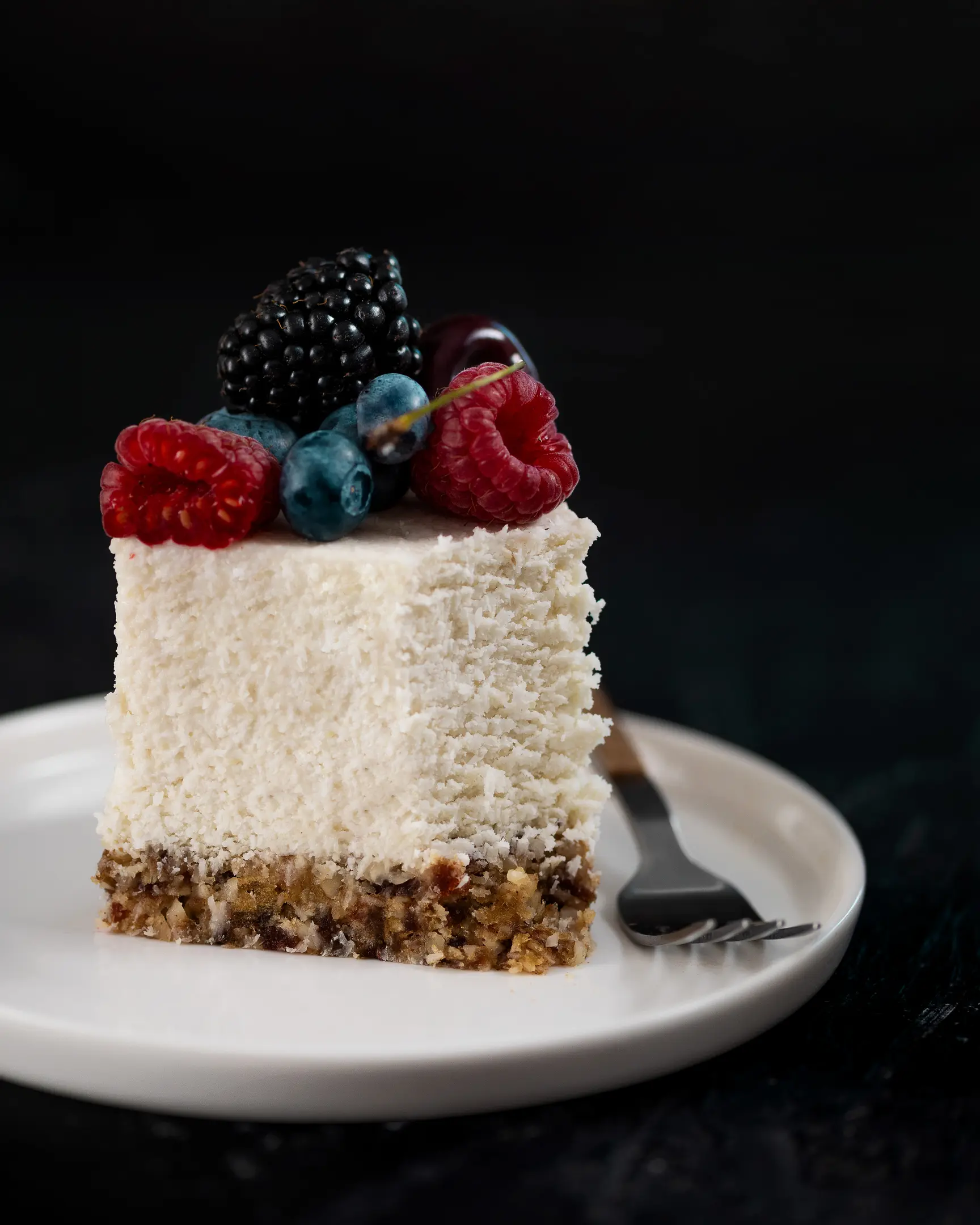 A piece of Coconut raw cake  A piece of Coconut raw cake  stand on a plate. Dark background 