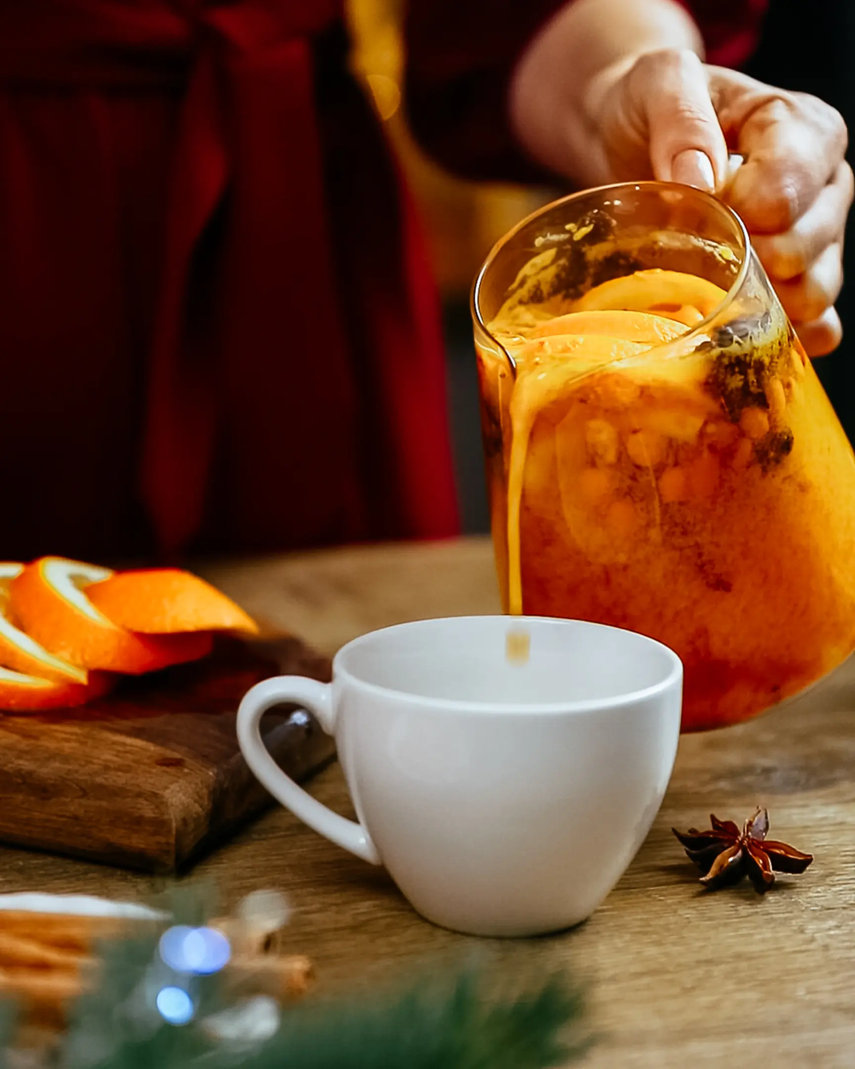 A woman in a burgundy dress on an orange-brown background pours sea buckthorn tea into a cup A woman in a burgundy dress on an orange-brown background pours sea buckthorn tea into a cup

