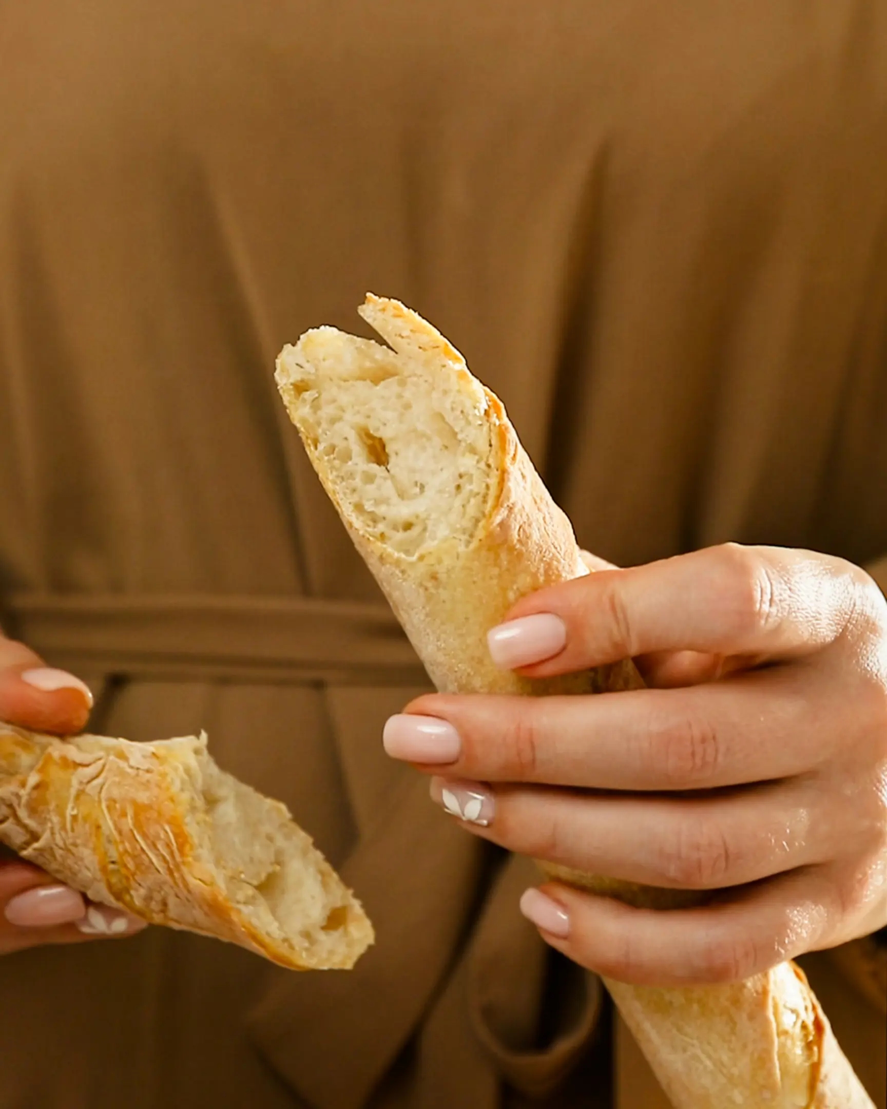 A woman in a beige dress holds a baguette in her hands A woman in a beige dress holds a baguette in her hands. She shows the texture of baguette 