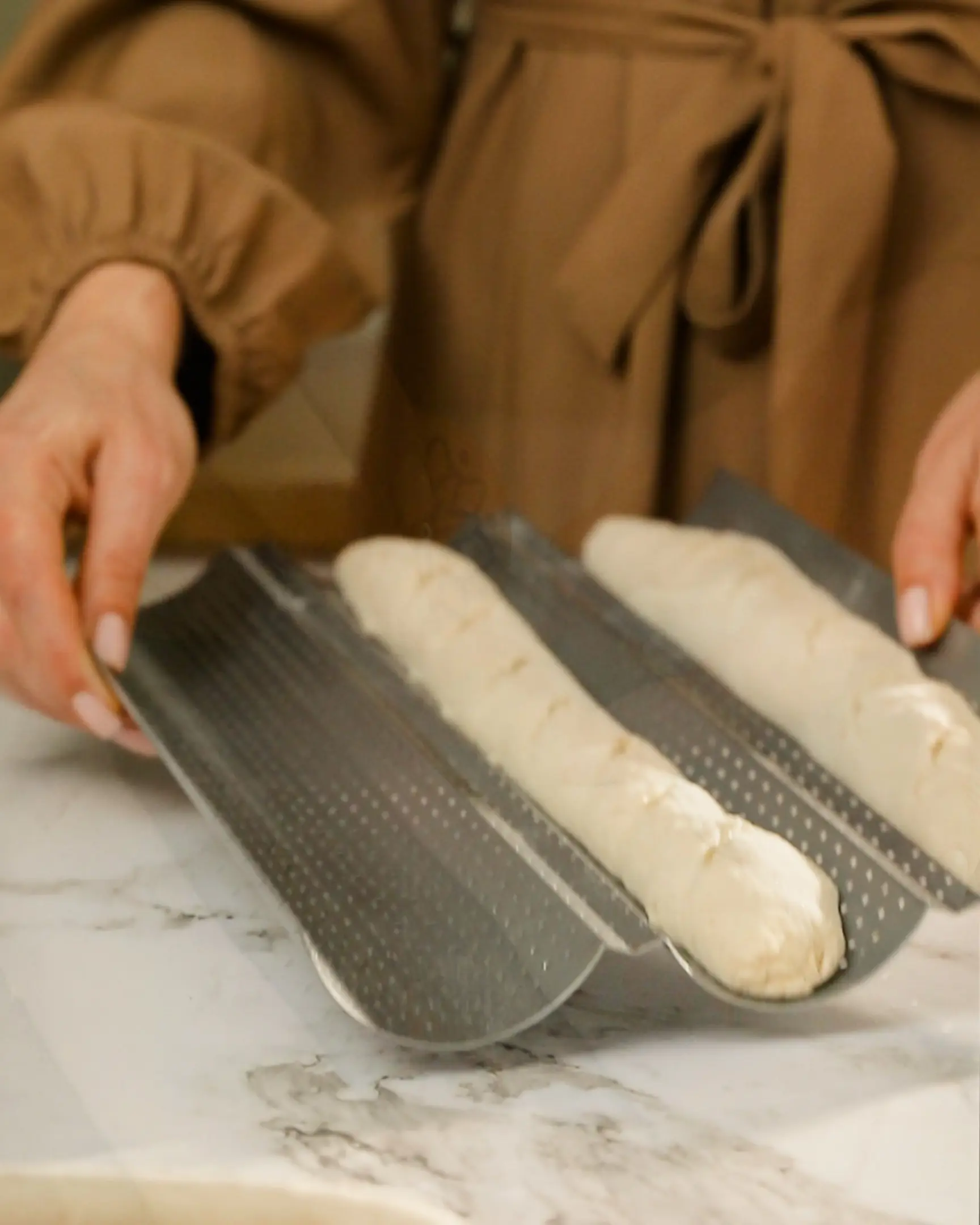 A woman takes baguette dough into the oven.  A woman takes baguette dough into the oven. The blanks are placed in special metal forms