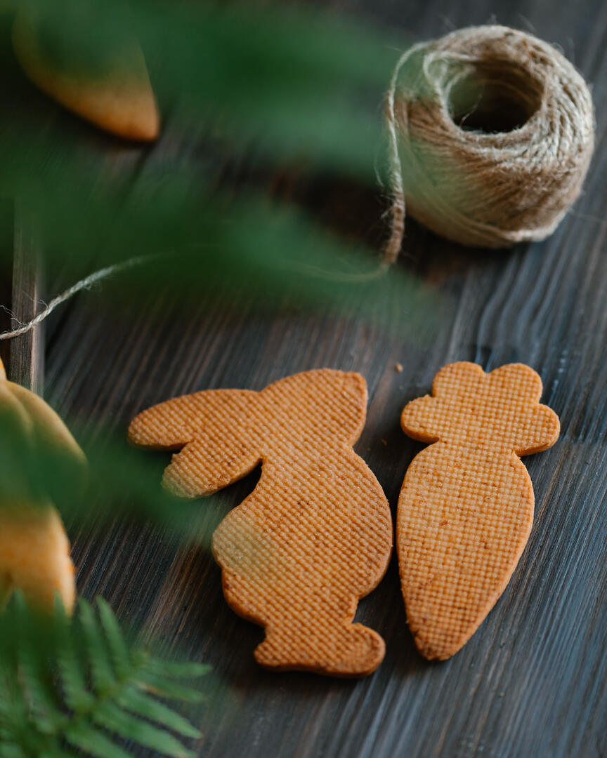 Pumpkin cookies in the shape of a hare. View from above. Hare-shaped cookies lie on a wooden surface in a wooden tray. There is moss and fern around - they imitate being in the forest. View from above.