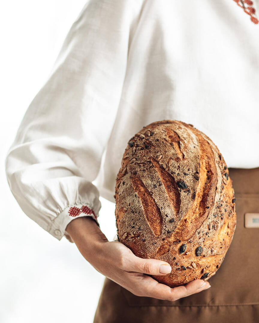 A woman dressed in shirt with national print holding the bread in her hands. A woman holding the bread in her hands.