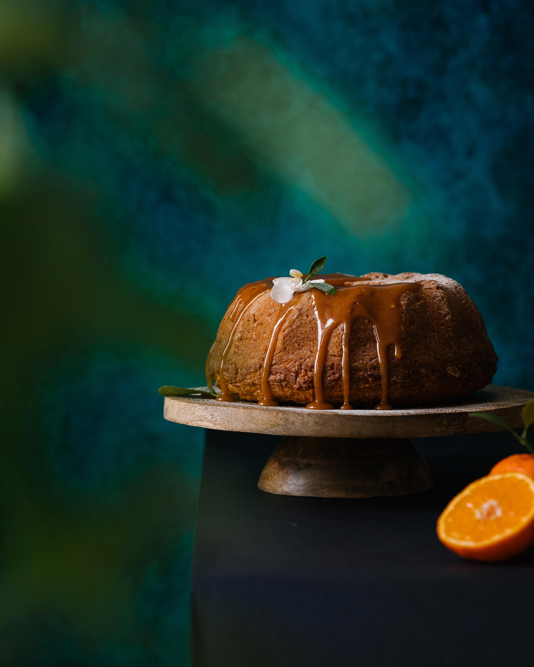 On a turquoise background, there is a cupcake with an orange . On a turquoise background, there is a cupcake with an orange on a wooden stand. There is an orange next to the cupcake. Plants are in the foreground of the frame in blur.