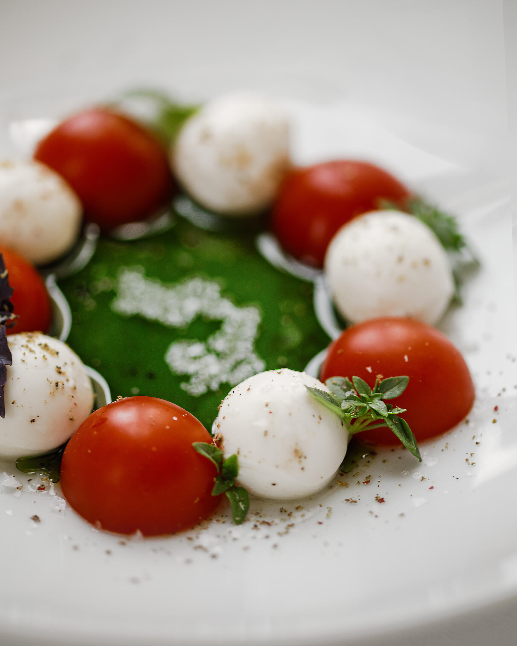 Caprese salad close-up. Caprese salad is served on a plate. It consists of green butter, mascarpone cheese, and tomatoes. Salad is located on a deep plate. The reflection of the window is visible on the plate.