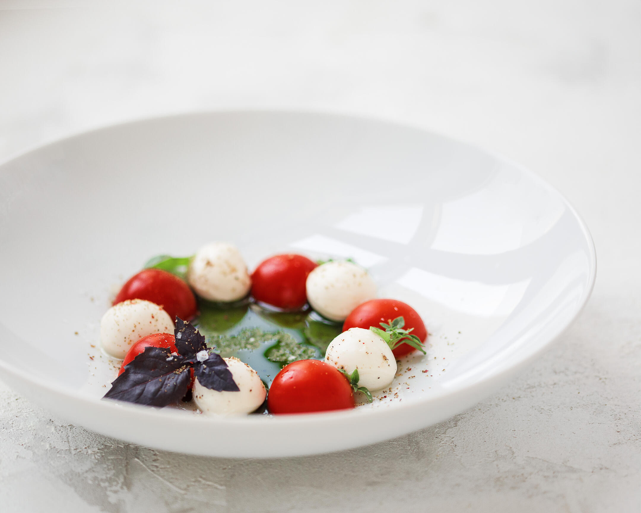 Caprese salad Caprese salad is served on a plate. It consists of green butter, mascarpone cheese, and tomatoes. Salad is located on a deep plate. The reflection of the window is visible on the plate.