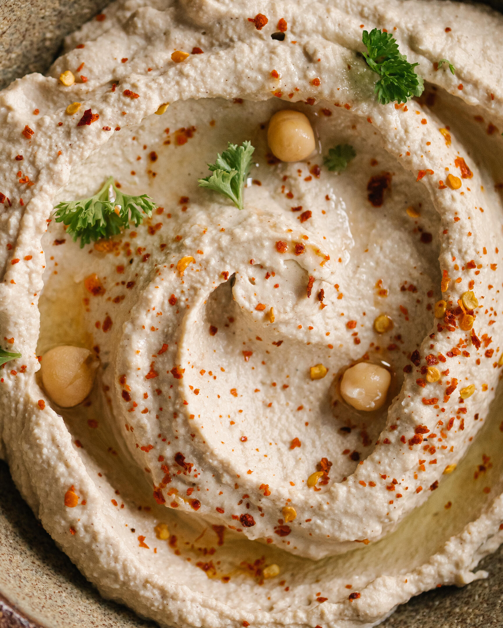 Humus texture view from above In the photo on the plate is hummus beautifully laid in a curl. Hummus is garnished with chickpeas and herbs.