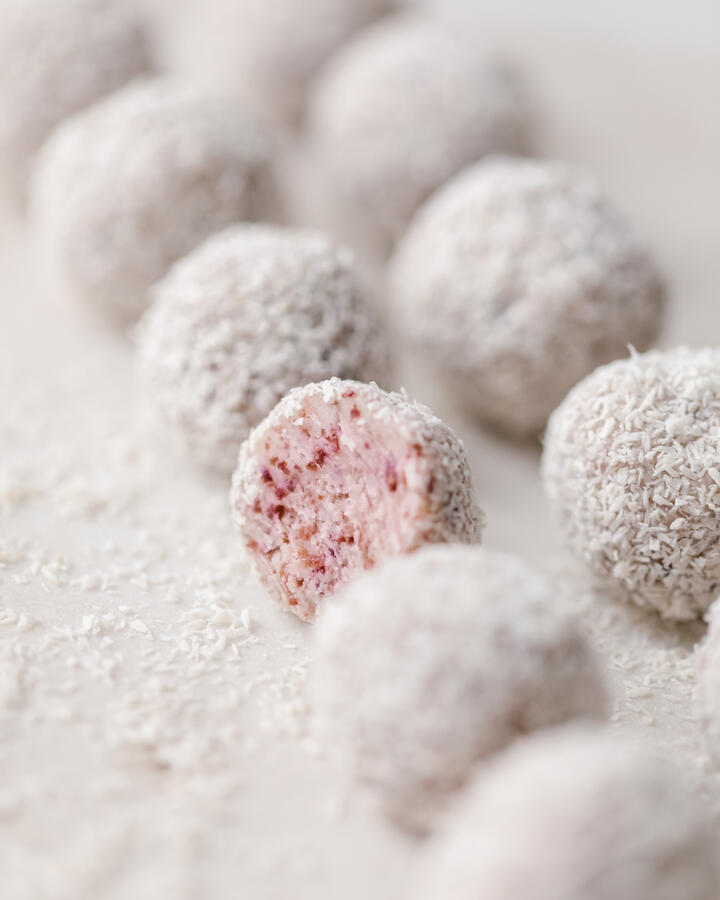 Truffles lie on a marble plate on a light background.  Truffles lie on a marble plate on a light background.  One of the truffles is cut open and you can see the texture with pieces of cranberries. Each truffle is covered in coconut flakes.