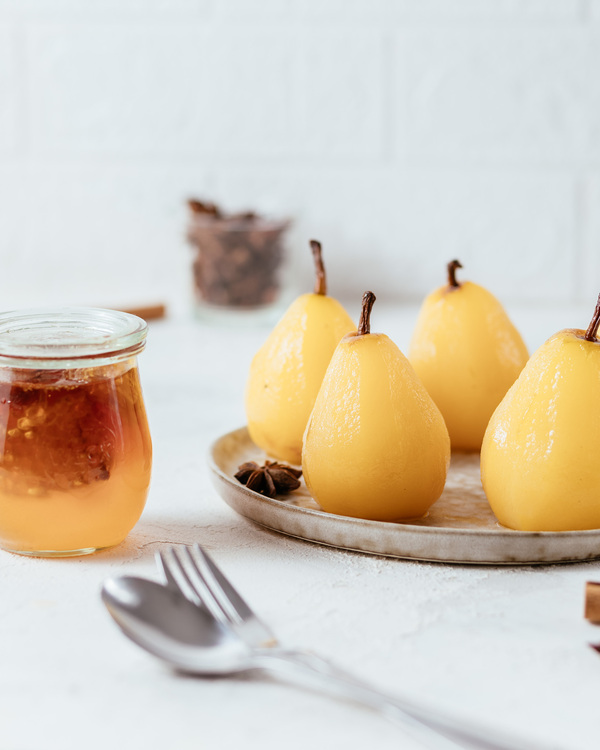Baked Pears And Honey. Baked Pears And Honey. Baked yellow pears are on a plate in the middle of the photo. On the left side of them, there is a jar with honey. A box is full of pecans in the background.