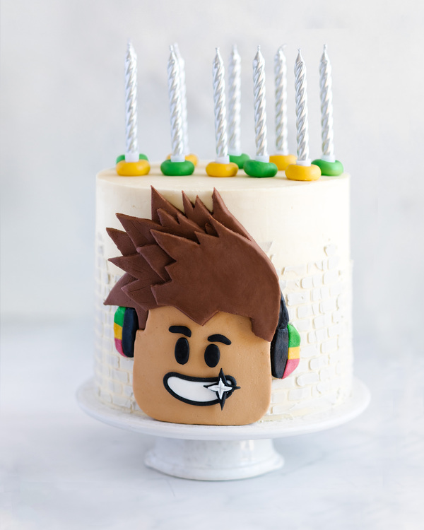 A cake for a boy. A cake for a boy. A white cake is in the middle of the photo and put on a pedestal of ceramics. On the top of it, there are candles. On the front side, there is a picture of a boy made of sugar.