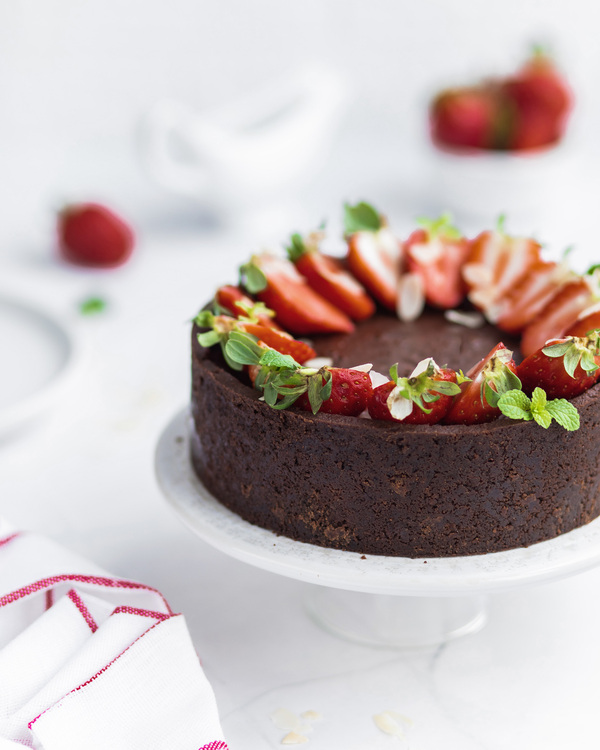 Round cake with strawberries. A round cake, topped with strawberries and mint, is in the middle of the photo.