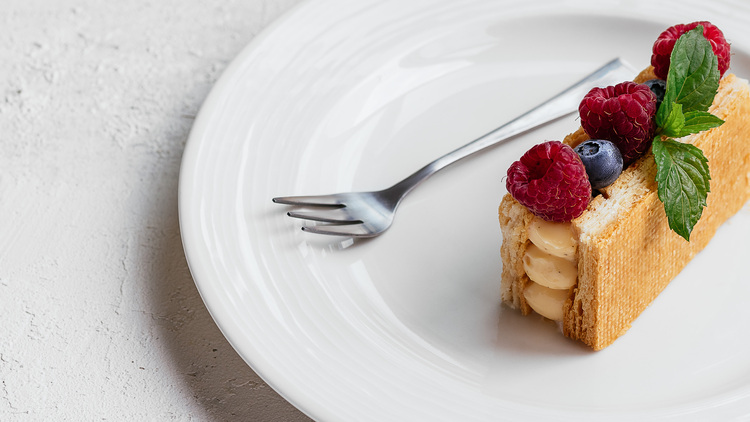 Eclair with vanilla cream. Eclair with vanilla cream topped with raspberries, blueberries, and mint is on a white plate.