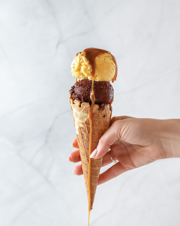 Ice Cream Savi Gelato. A person is holding a con with the chocolate and mango ice cream in the middle of the photo.