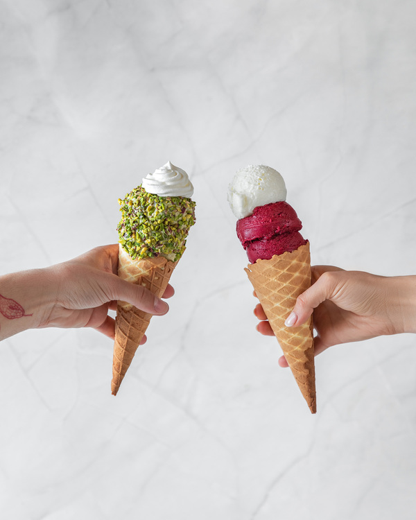 Ice Cream Savi Gelato. Two cons with the ice cream are in the middle of the photo. The con with pistachio ice cream decorated with crashed pistachios is on the left. The con with vanilla and blueberries ice cream is on the right.