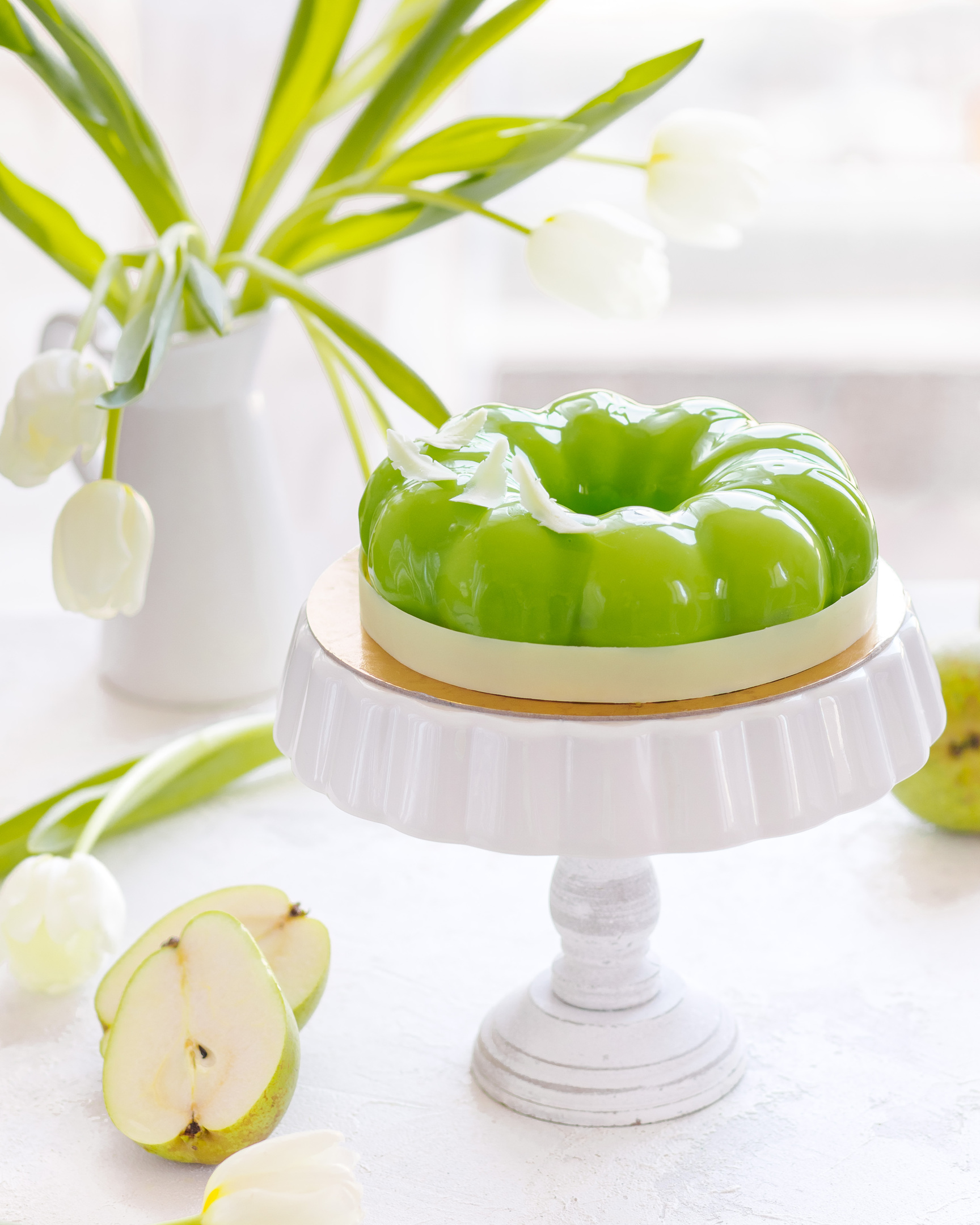 Round Pears Cake. Round Pears Cake on a pedestal made of white ceramic in the middle of the photo. Green pears on the left side and white flowers in the background!