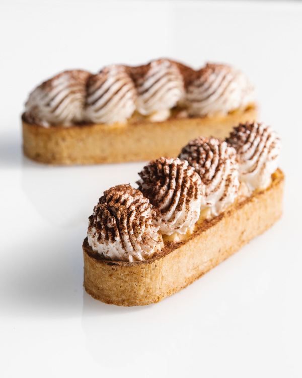 Vegan eclairs with coconut cream and cacao. Two eclairs topped with cacao are in the center of the photo with a white background.