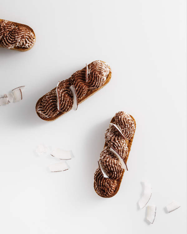 Vegan eclairs with coconut cream. Vegan eclairs with coconut cream. Two eclairs topped with cacao and coconut pieces are in the center of the photo with a white background.