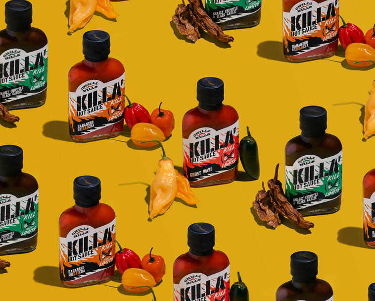На жълт фон има бутилки Chilli Hills Killa с различни вкусове. На жълт фон има бутилки Chilli Hills Killa с различни вкусове. До всяка бутилка има чушки, които демонстрират основния компонент на соса.