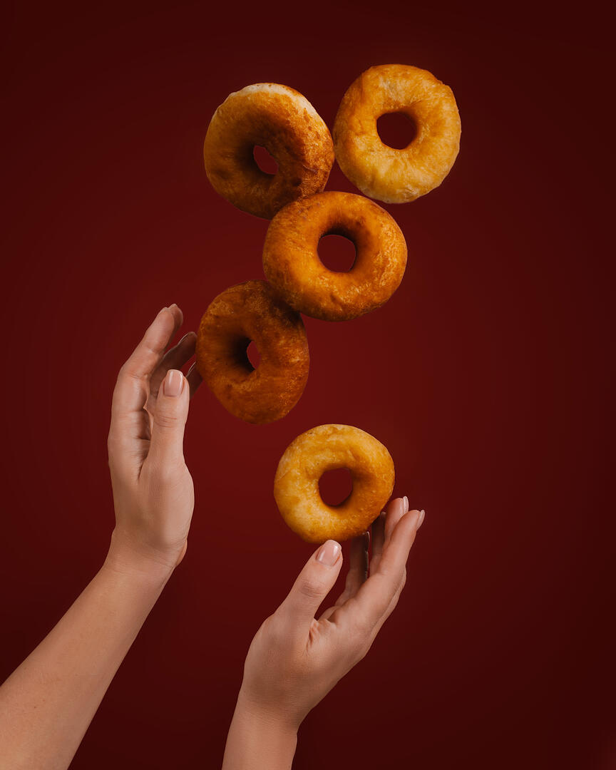 Donuts hung in the air. The photo shows female hands and donuts flying in the air above them.