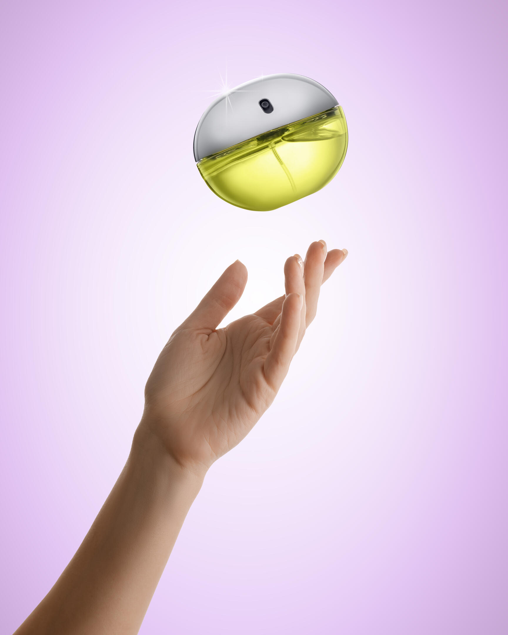 Be Delicious Eau de Parfum DKNY perfume with purple background. Be Delicious Eau de Parfum DKNY perfume levitates in the air above a woman's hand on a light purple background.