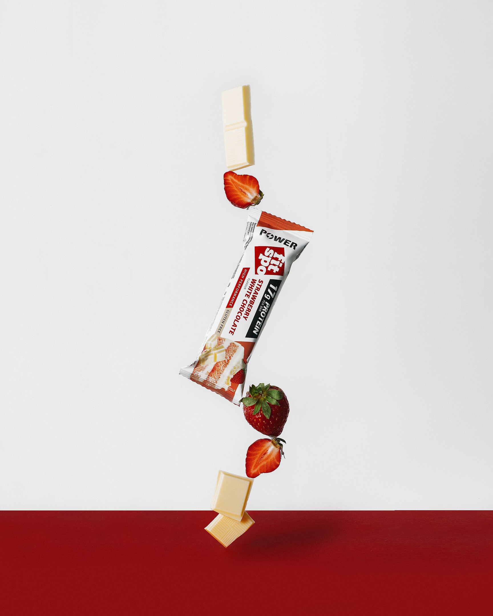 Fitpro bar балансира, сред ягоди и парчета шоколад Fitpro бар балансира, стоящ върху парче бял шоколад и ягоди. На върха на бара има също ягоди и парчета шоколад.