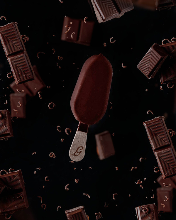 Ice Cream in free fall flies among small pieces chocolate chips and dark chocolate pieces. Ice Cream in free fall flies among small pieces chocolate chips and dark chocolate pieces. Ice Cream in free fall flies among small pieces of chocolate dust and dark chocolate pieces. On the dark background.