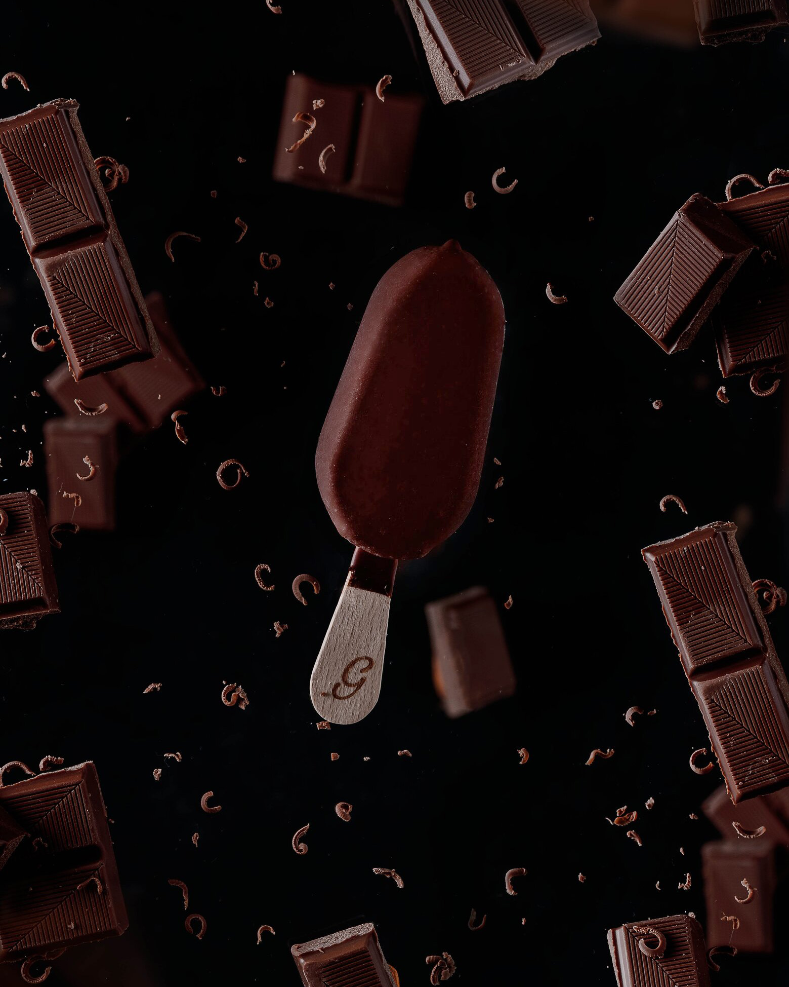 Ice Cream in free fall flies among small pieces chocolate chips and dark chocolate pieces. Ice Cream in free fall flies among small pieces of chocolate dust and dark chocolate pieces. On the dark background.