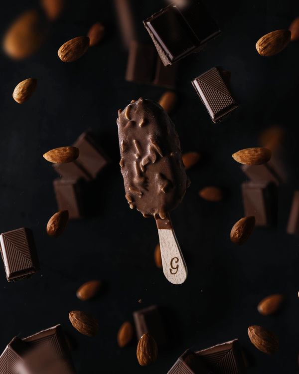 Ice Cream in free fall flies among almond nuts and dark chocolate pieces. Ice Cream in free fall flies among almond nuts and dark chocolate pieces. On the dark background.