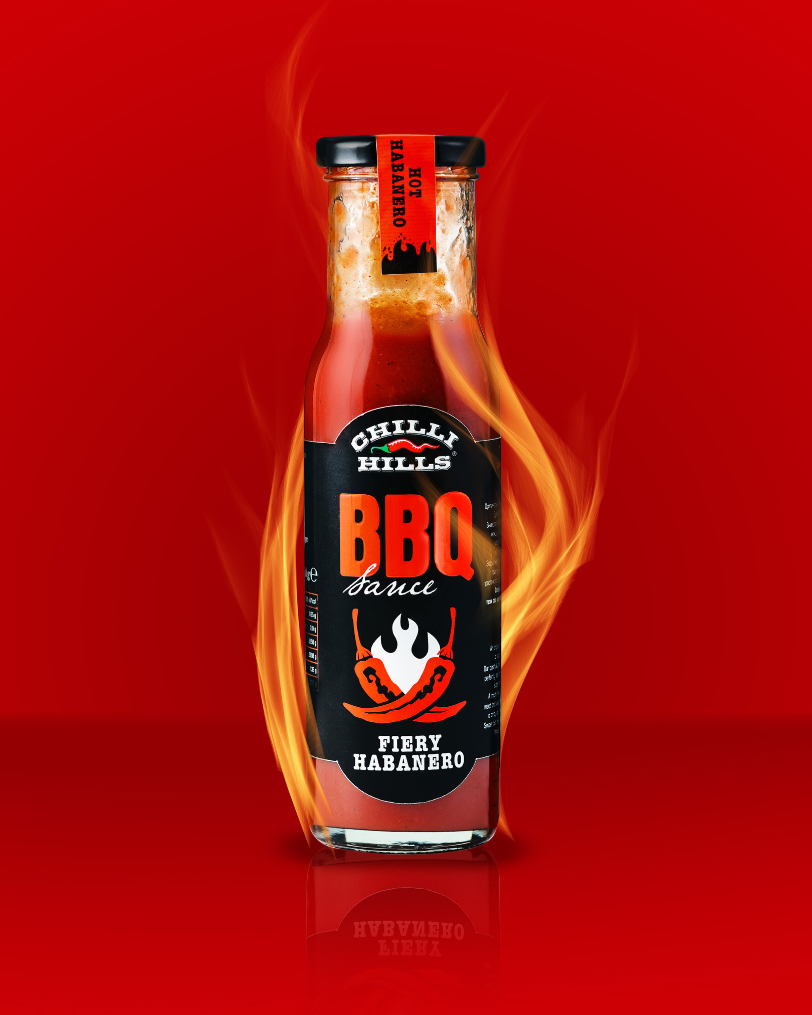 Ketchup BBQ Chilli Hills Bottle On Fire. The illusion that a bottle of ketchup BBQ Chilli Hills bottle standing on fire. The bottle stands on a red background, there is a reflection from the bottom of the bottle, which informs the viewer that the ketchup is on a glossy reflective surface under the bottle. 