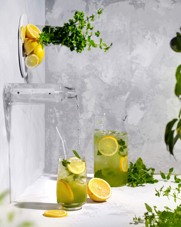 Lemonade and horizontal water illusion. The illusion that a bottle is on the wall horizontally and the water is pouring into a glass full of lemonade with lemons and mint. Another glass of lemonade in the gray background. Lemons and mint are everywhere!