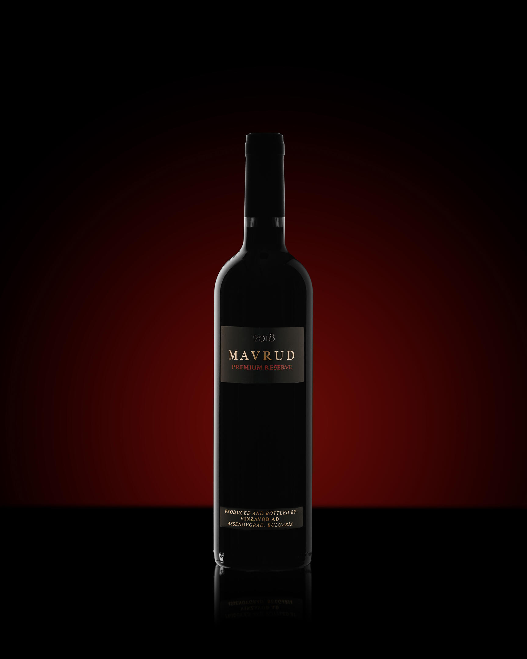 A bottle of 2018 Mavrud Premium Reserve wine on a dark background with HARG highlights. A bottle of 2018 Mavrud Premium Reserve wine on a dark background with HARG highlights in the left part of the bottle. Reflection is located at the bottom of the bottle.   In the background, behind the bottle, there is a red backlight that separates the bottle from it. 